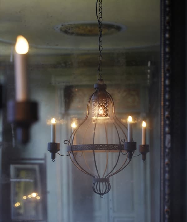 Un lustre à quatre branches suspendu dans une pièce aux tons crème, avec une porte ornée à l'arrière-plan.