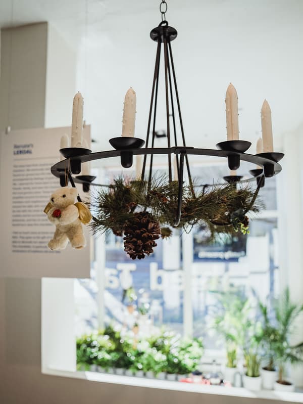 Un lustre LERDAL suspendu au plafond est en présentation et des feuilles d’arbres, des pommes de pin et une peluche y sont attachées.