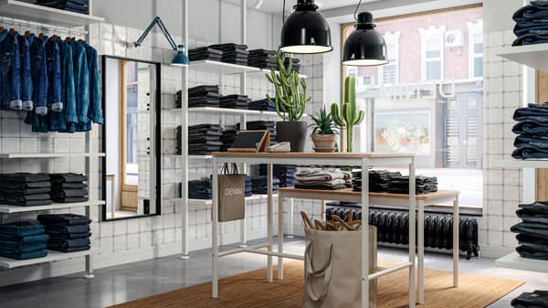 Un magasin de pantalons en denim avec des piles de jeans pliés et d’autres vêtements sur un agencement ELVARLI et des tables TOMMARYD.