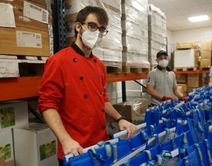 Un magatzem amb dos treballadors de cuina preparant menjar dins de bosses refrigerants blaves d’IKEA.