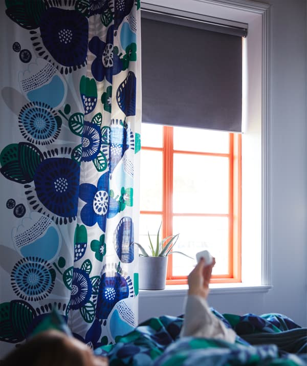 Un mando a distancia sen fíos que funciona a pilas, baixando un estor opaco IKEA FYRTUR gris.