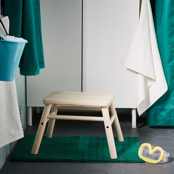 Un marchepied en bouleau est posé sur un tapis de bain à proximité du meuble lavabo.