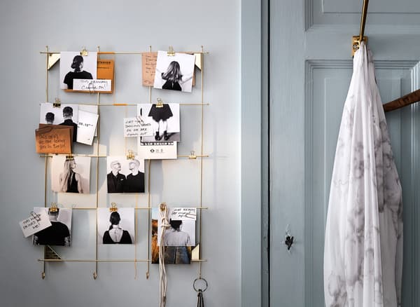 Un marco de arame de latón IKEA MYRHEDEN empregado como calendario de parede de actividades de manualidades, con fotos e notas enganchadas no marco.