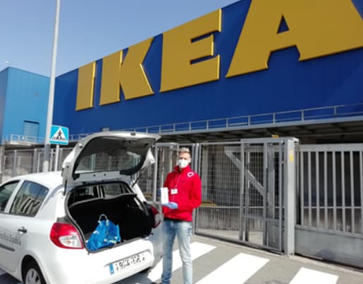 Un metge vestit de vermell davant d’una botiga IKEA, amb el cotxe estacionat al costat.