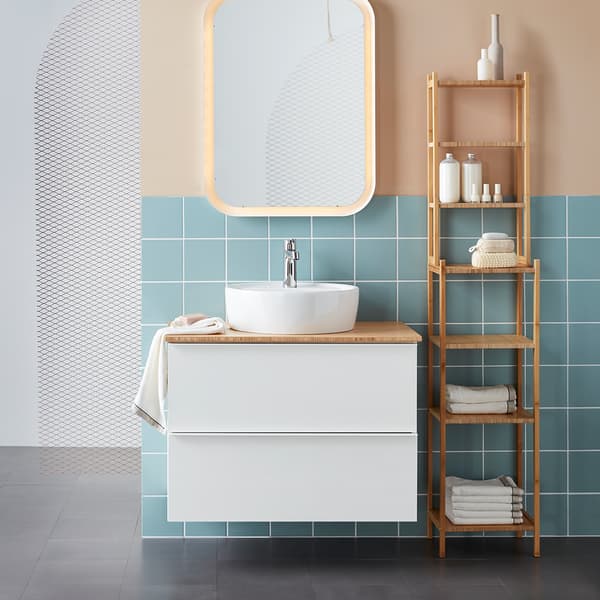 Un meuble de salle de bains blanc avec un lavabo rond sur le comptoir, à côté d'une étagère en bambou. 