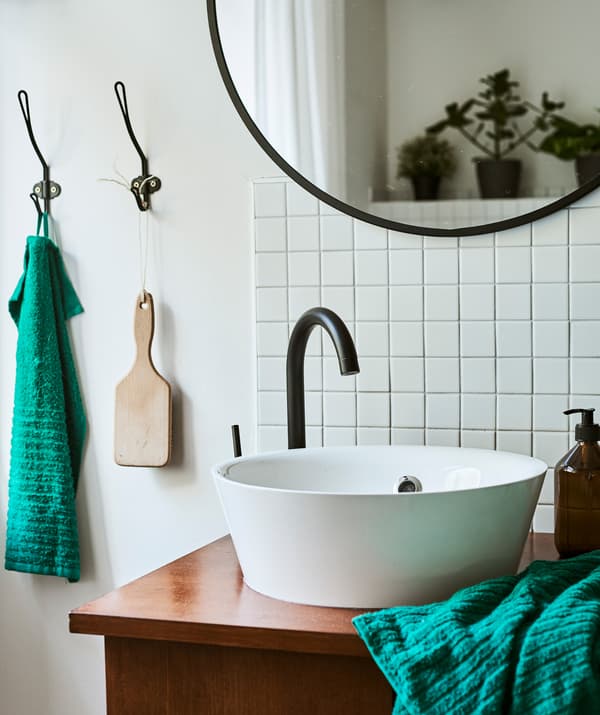 Un meuble lavabo unique associant un lavabo moderne blanc avec un meuble vintage, à côté de carreaux style métro et un miroir noir rond.