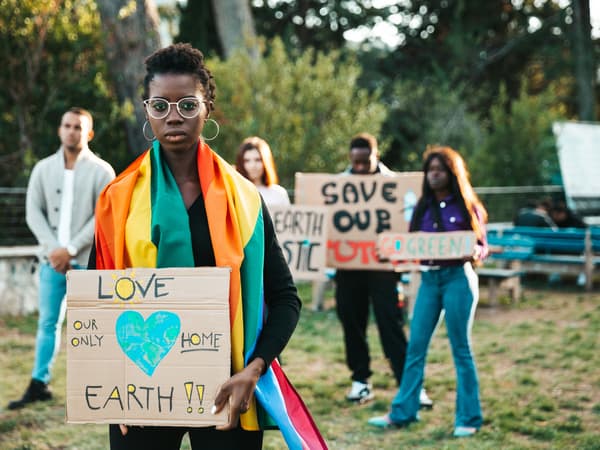 Un mic grup de activiști climatici țin în mână pancarte din carton maro scrise de mână, la un protest pașnic într-un parc.