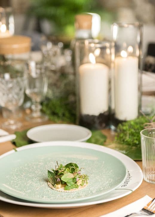 Un mini taco di salmone in un piatto verde. La tavola è allestita con candele accese in vasi di vetro, bicchieri e accessori di colore verde.
