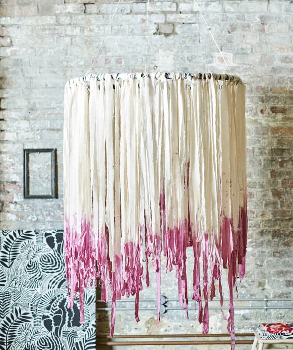 Un mobile de style boho pend près d’un mur. Le cerceau est décoré de longues bandelettes de tissu blanc pendantes, teintes en rose aux extrémités.