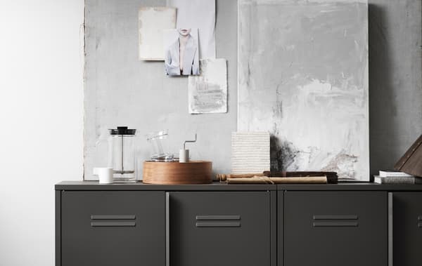 Un mobile in acciaio con ante IVAR davanti a una parete grigia. Sopra il mobile ci sono una caffettiera/teiera pressofiltro e altri oggetti decorativi.