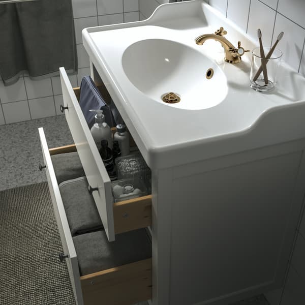 Un mobile per bagno con lavabo. Ha due cassetti aperti e lascia intravedere accessori e tessili da bagno.