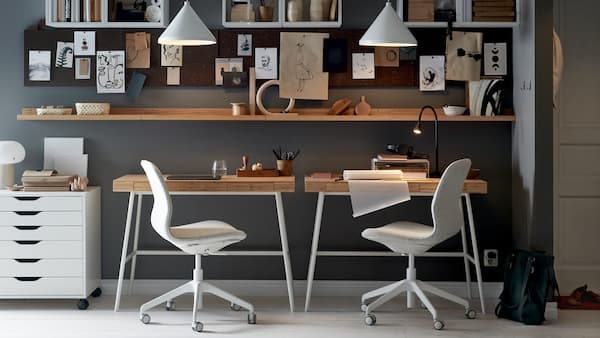 Un mur avec deux bureaux LILLÅSEN, des chaises de bureau et un caisson à tiroirs, avec des tablettes, des tableaux d’affichage et des suspensions blanches.