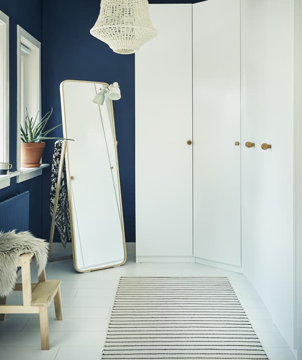 Un mur de garde-robes blanches et un miroir dans une pièce bleu foncé.