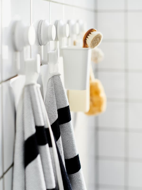 Un mur de salle de bains carrelé avec une rangée de crochets à ventouse TISKEN où sont accrochées des serviettes et une brosse.