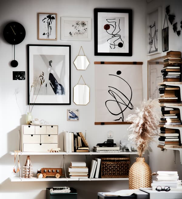 Un mur décoratif avec des cadres, boîtes, livres, une horloge, des jouets et un vase – le tout en noir, blanc et nuances marron.