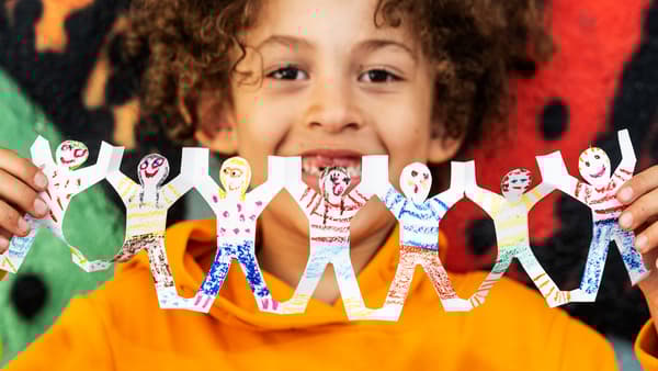 Un nen amb una dessuadora taronja subjecta garlandes de paper decorades de nens i nenes agafats de les mans.