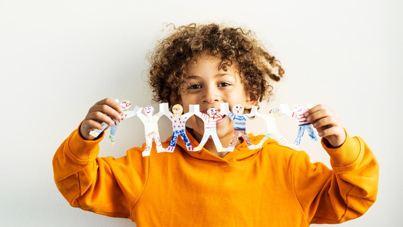 Un nen amb una dessuadora taronja subjecta una garlanda decorada molt divertida de nens i nenes agafats de les mans.