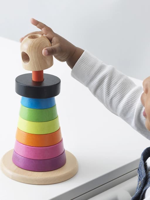 Un nen petit juga amb anells d’apilament de fusta de diversos colors.