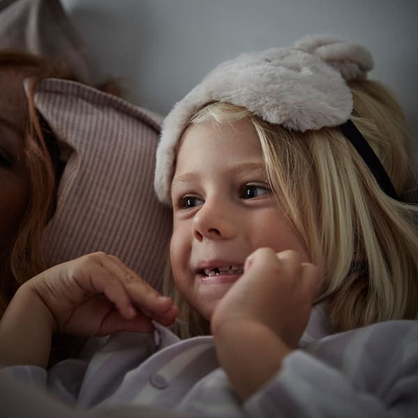 Un neno pequeno co pelo louro e longo e cun anteface peludo na parte superior da cabeza está apoiado nunha almofada suave.