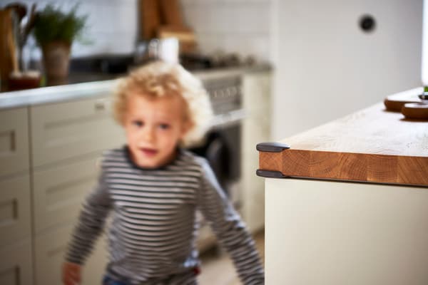 Un niño corriendo en una cocina, se ve en detalle el borde de la mesa con un protector de seguridad.