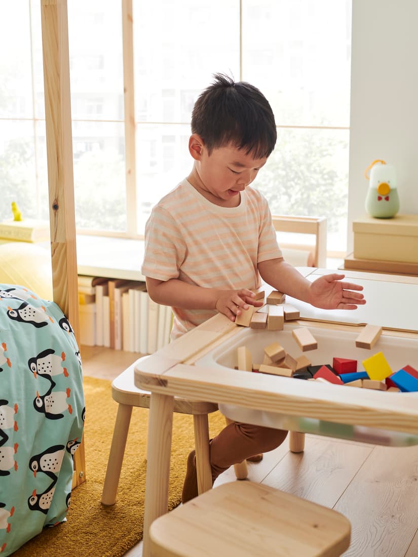 Un niño parado al costado de una mesa FLISAT con bloques de colores.