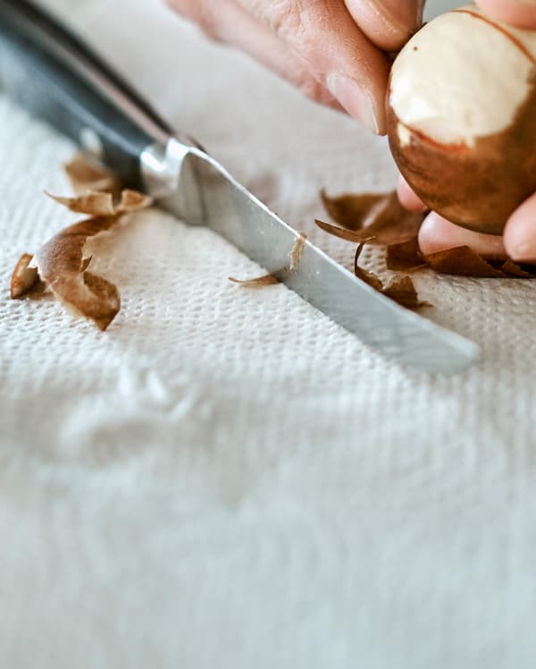 Un noyau d’avocat dont on pèle la peau sur un essuie-tout à côté d’un couteau de cuisine avec un manche noir.