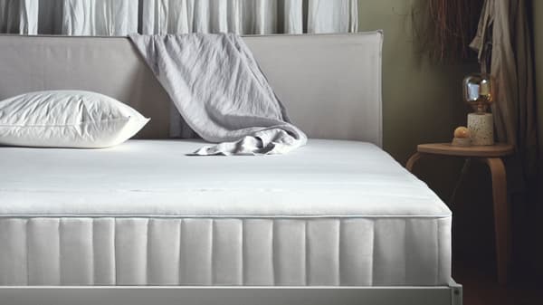 Un oreiller LAPPTÅTEL placé en position basse sur un matelas ferme à ressorts ensachés VESTERÖY bleu clair, sur une structure de lit.