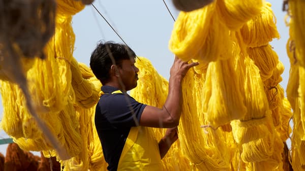 Un ouvrier textile en Inde suspend du coton fraîchement teint en jaune vif pour le faire sécher.