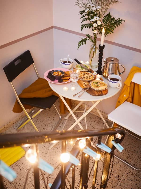 Un palier d’escalier avec des chaises GUNDE et une petite table, sur celle-ci une planche à découper FASCINERA avec des aliments, des fleurs et du café.