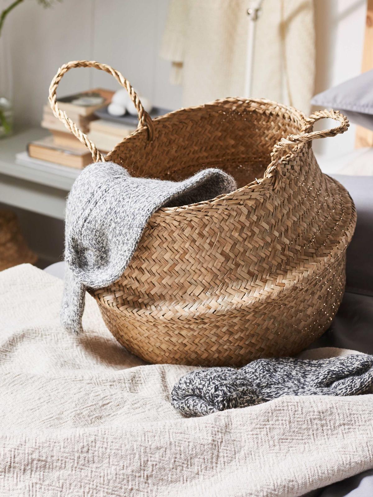 Un panier en jonc de mer beige posé sur un lit avec une paire de chaussettes grises à l’intérieur.