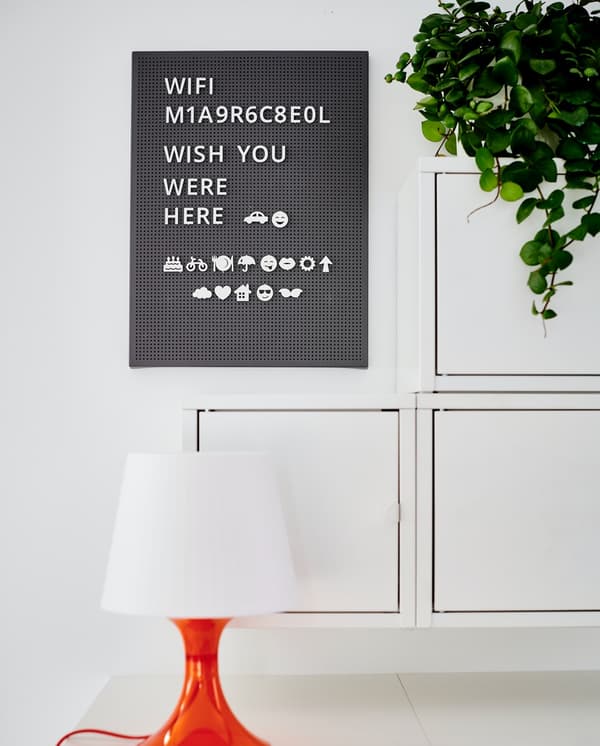 Un pannello perforato SVENSÅS con delle scritte sopra. Accanto e sotto un mobile EKET da parete. Davanti al mobile EKET è posta una lampada appoggiata a un mobile.