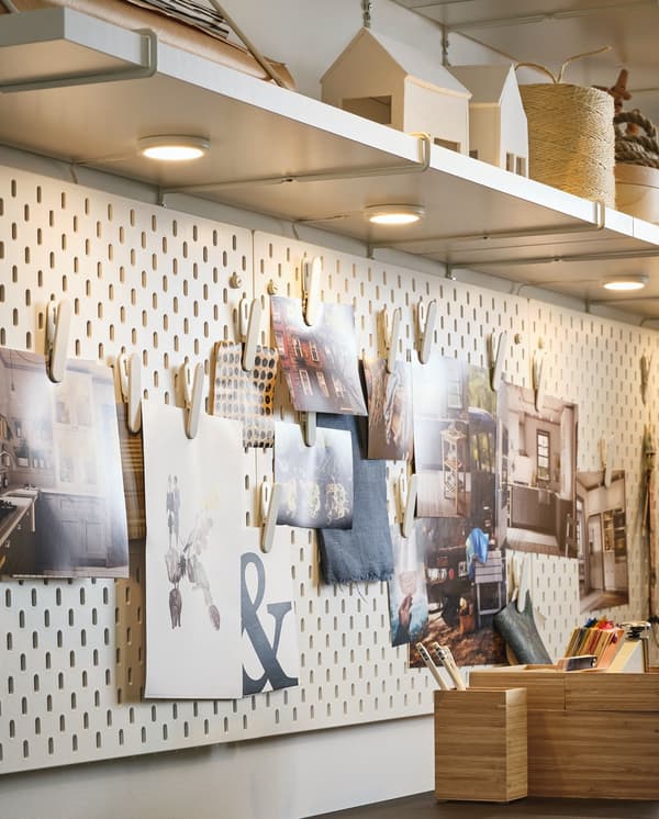 Un pannello portaoggetti bianco con tante foto e immagini di ispirazione, illuminato da faretti rotondi fissati sotto una mensola bianca. 