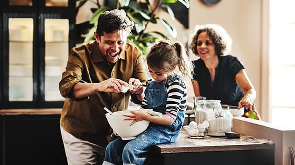Un papà e una mamma che stanno insegnando alla propria figlia a cucinare.
