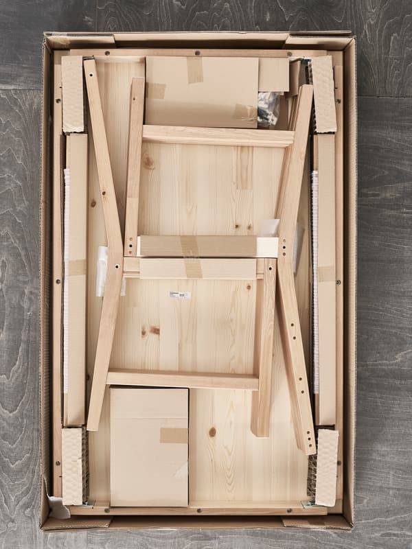 Un paquet plat IKEA ouvert, montrant les éléments d’une chaise en pin à assembler.