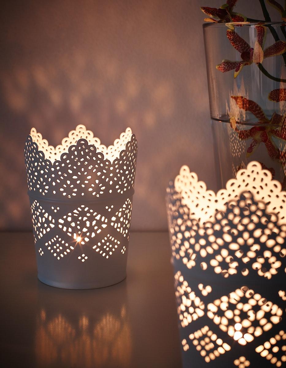Un par de velas encendidas en los portavelas IKEA SKURAR. Se aprecia como a través de las rendijas de los portavelas se filtra la luz hacia las paredes y la mesa.