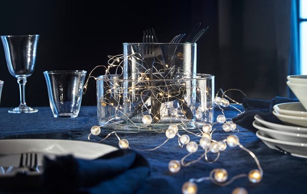 Un parell de cadenes d’il·luminació LED IKEA SNÖYRA  estirades sobre una taula entre gots i plats.