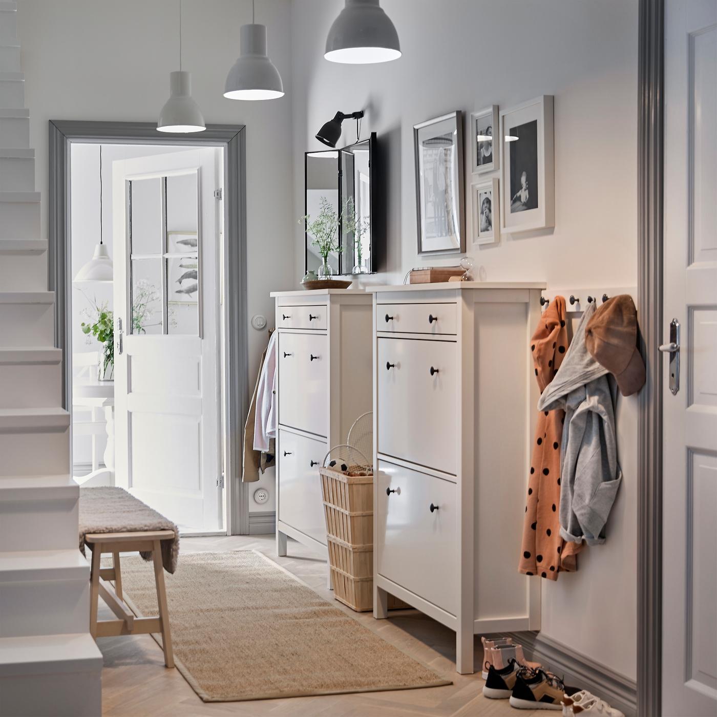 Un pasillo blanco con dos zapateros tradicionales de HEMNES uno al lado del otro y una fila de ganchos para abrigos.