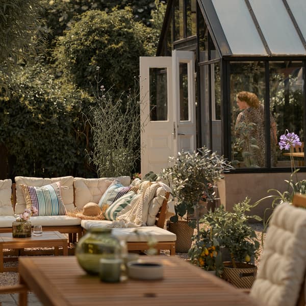 Un patio con un sofá modular de exterior en marrón claro con cojines en beige y una mesa de exterior en marrón claro con una silla reclinable.
