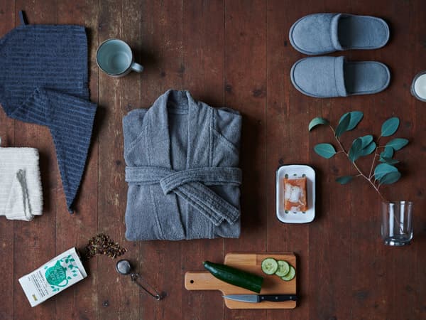 Un peignoir, une serviette de toilette, une pantoufle et une tasse de thé posés sur un sol en bois.