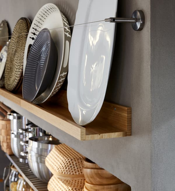 Un perete cu corpuri de depozitare decorative cu o poliță pentru fotografii din lemn pe care sunt expuse farfurii și tăvi, toate în tonuri de alb, gri și maroniu.