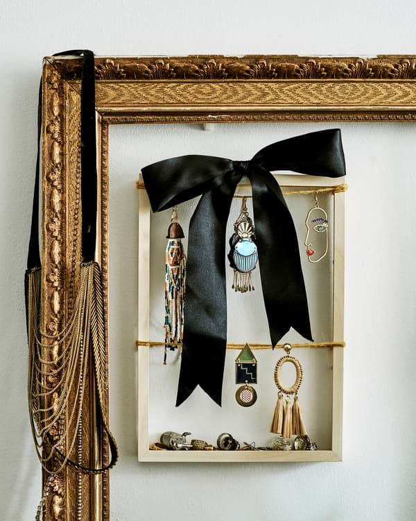 Un petit cadre en bois utilisé pour exposer des boucles d’oreilles pendantes et un ruban noir, placé à l’intérieur d’un grand cadre doré.
