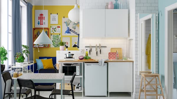 Un petit coin cuisine lumineux aménagé avec une combinaison de cuisine ENHET blanche, une table blanche et quatre chaises noires.