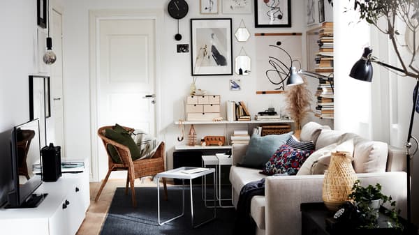 Un petit salon avec beaucoup de lumière, un canapé, un téléviseur, un présentoir à livres vertical et un mur artistique, le tout dans des couleurs neutres.
