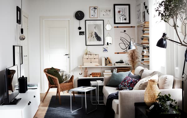 Un petit séjour très lumineux, avec un canapé, une TV, un présentoir à livres vertical et une galerie murale, le tout dans des tons neutres.