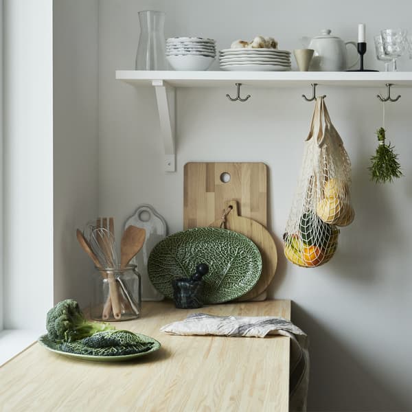 Un piano di lavoro in legno con piatto da portata a forma di foglia, taglieri in legno e stoviglie su una mensola.