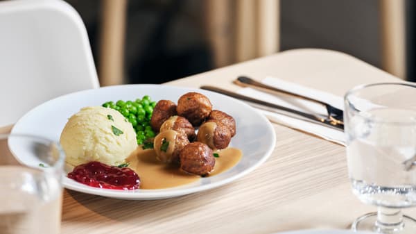 Un piatto con polpette, piselli, purè e salsa ai mirtilli su una tavola. 