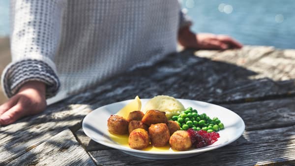 Un piatto di polpette di pesce con purè e piselli su un tavolo. Sullo sfondo, una persona e il mare. 