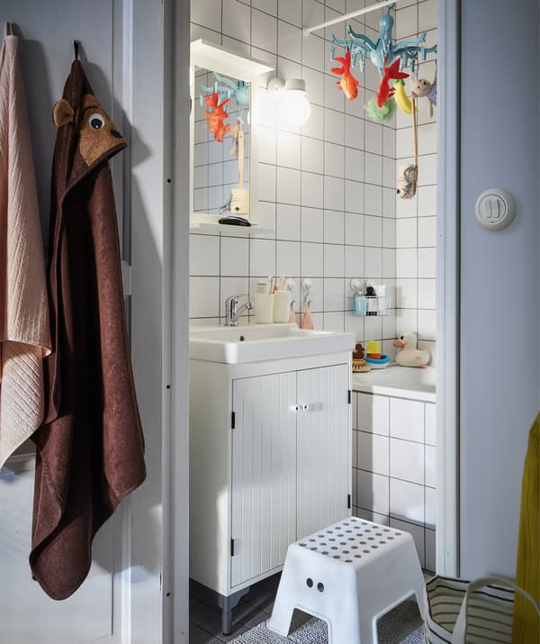 Un piccolo bagno con piastrelle bianche e una scaletta/sgabello davanti al lavabo - IKEA