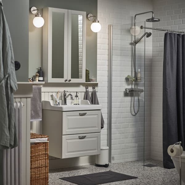 Un piccolo bagno con un mobile a specchio bianco, un mobile per lavabo grigio, un tappeto per bagno grigio scuro e una tenda doccia antracite - IKEA