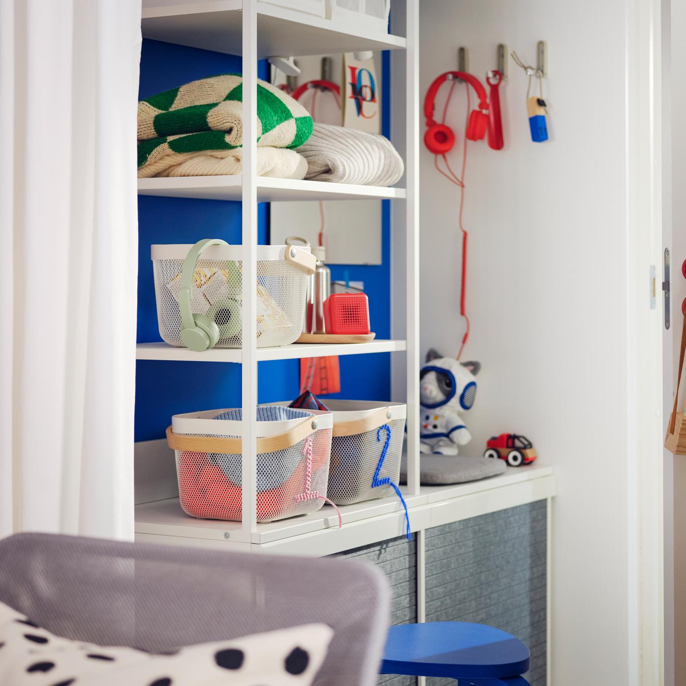 Un piccolo ingresso in stile scandivano con un guardaroba PLATSA a giorno bianco, sui cui ripiani sono sistemati cestini e vestiti, contro una parete blu - IKEA.